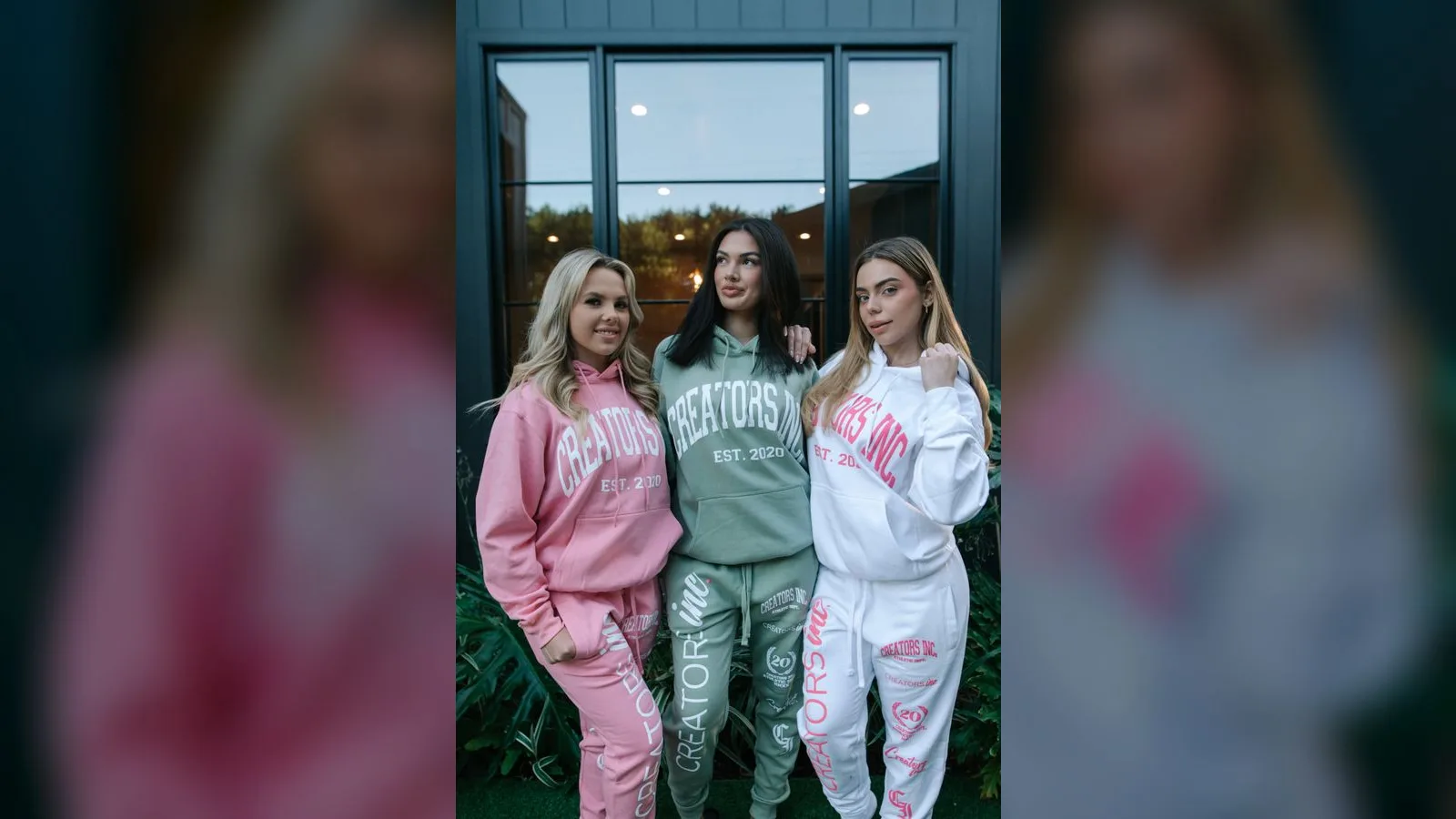 Three creators standing arm in arm in pink, green and white Creators Inc branded hoodies outside a modern home