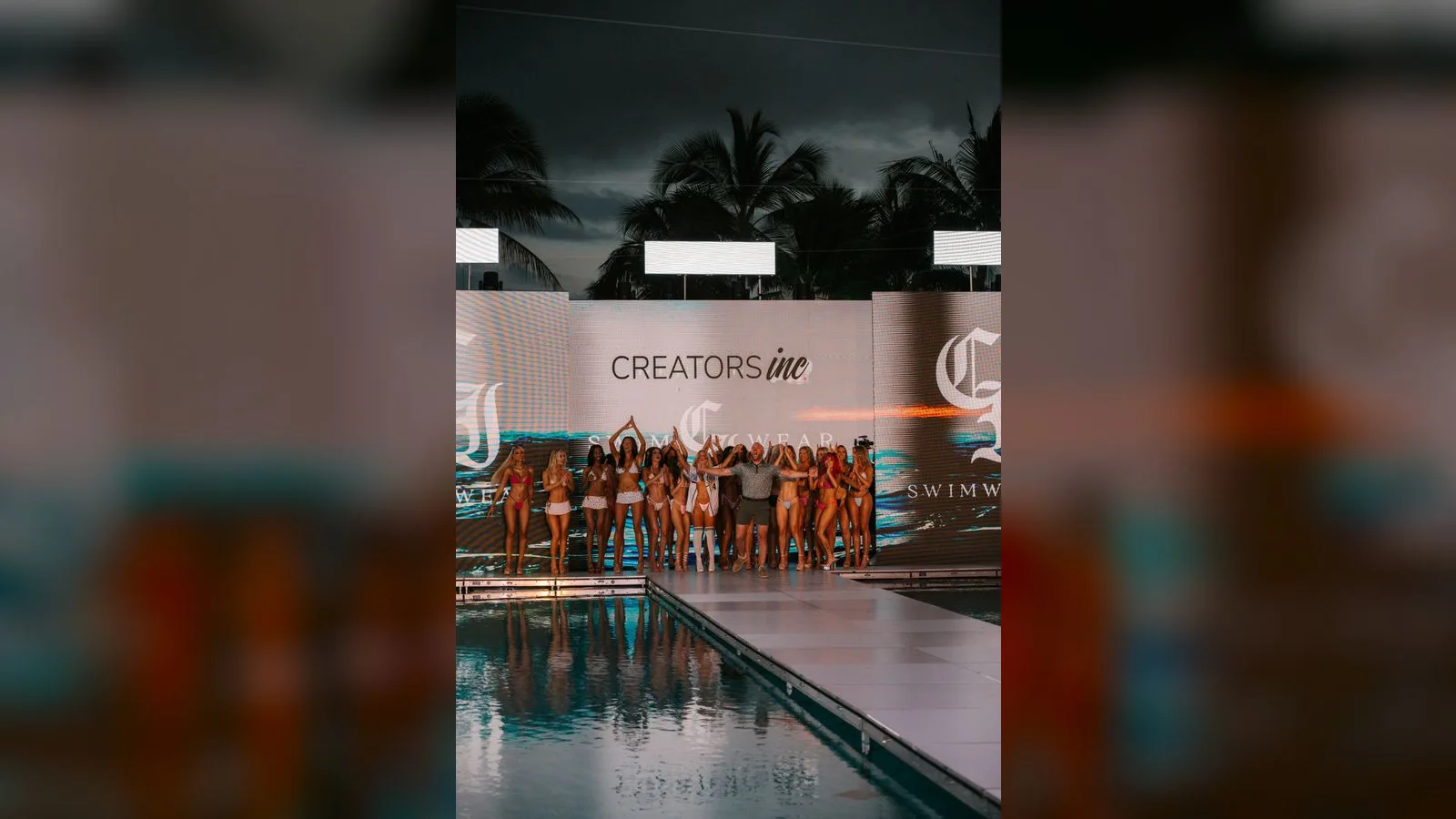 Lineup of creators on the poolside runway stage at the Creators Inc swimwear show with branded screens behind them